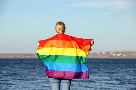 Woman holding bright LGBT flag near river, back viewの写真素材