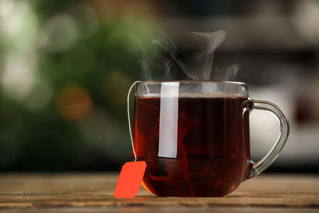 Tea bag in glass cup of hot water on wooden table against blurred backgroundの写真素材