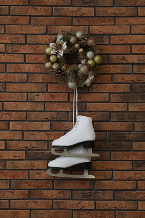 Pair of ice skates and beautiful Christmas wreath hanging on brick wallの写真素材