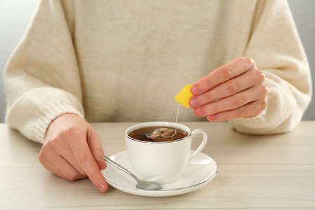 Woman dipping tea bag into cup of water at white wooden table, closeupの写真素材