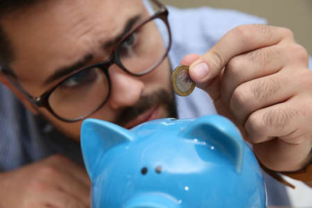 Young man putting coin into piggy bank, focus on hand. Money savingsの写真素材