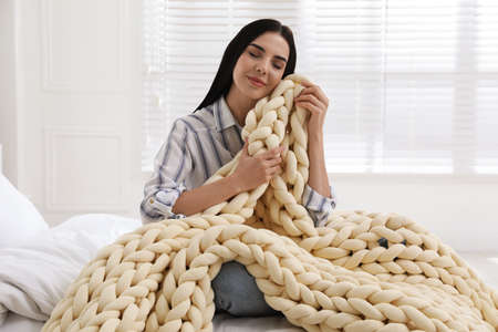 Young woman with chunky knit blanket on bed at homeの写真素材