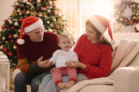 Happy couple with cute baby on sofa in room decorated for Christmas