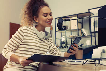 African American woman with smartphone working as radio host in modern studioの写真素材