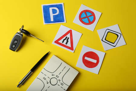 Flat lay composition with workbook for driving lessons and road signs on yellow background. Passing license examの写真素材