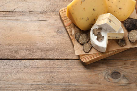 Board with delicious cheeses and fresh black truffles on wooden table, top view. Space for textの写真素材
