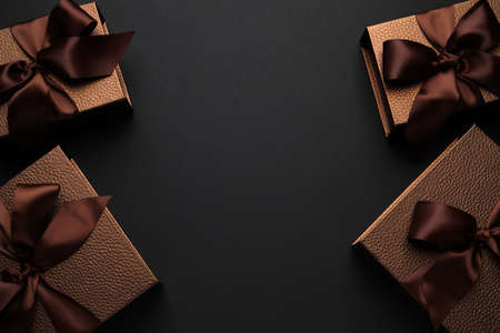 Brown gift boxes decorated with satin bows on black background, flat lay. Space for textの写真素材
