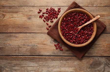 Raw red kidney beans with bowl, spoon and napkin on wooden table, flat lay. Space for text