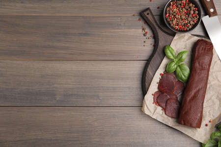 Delicious dry-cured beef basturma with basil and peppercorns on wooden table, flat lay. Space for textの写真素材
