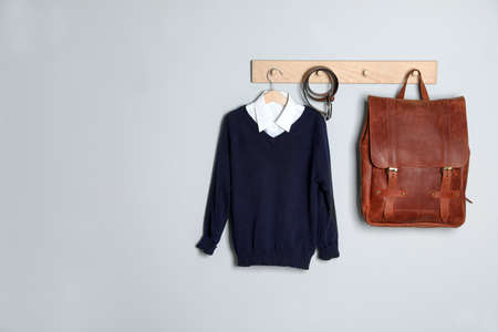 Shirt, jumper and bag hanging on white wall. School uniform. Space for textの写真素材