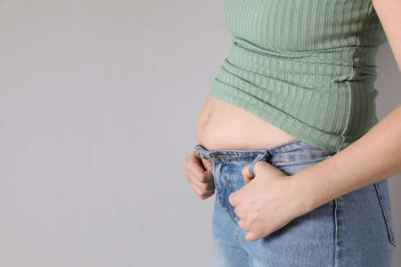 Woman wearing tight clothes on light gray background, closeup view with space for text. Overweight problemの写真素材