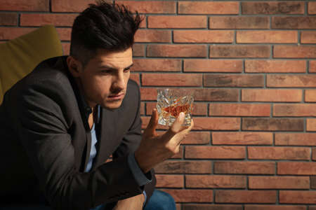 Addicted man with glass of alcoholic drink near red brick wallの写真素材