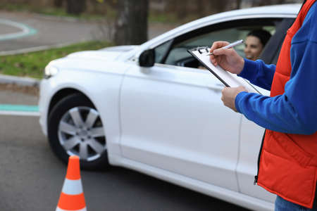 Instructor with clipboard near car outdoors, closeup. Driving school examの写真素材