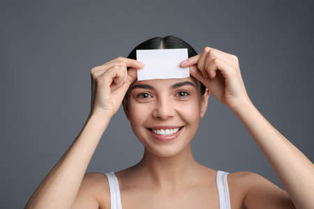 Beautiful woman using mattifying wipe on gray backgroundの写真素材
