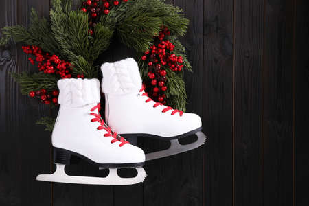 Pair of ice skates and beautiful Christmas wreath hanging on dark wooden wall, space for textの写真素材