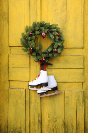 Pair of ice skates and Christmas wreath hanging on old yellow doorの写真素材