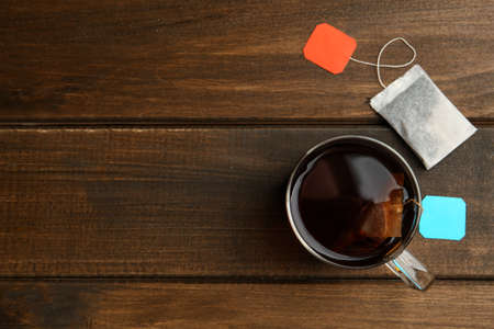 Tea bags in glass cup of hot water on wooden table, flat lay. Space for textの写真素材