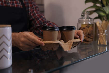 Barista putting takeaway coffee cups with cardboard holder on glass table in cafe, closeupの写真素材