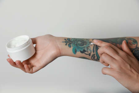 Woman applying cream on her arm with tattoos against light background, closeupの写真素材
