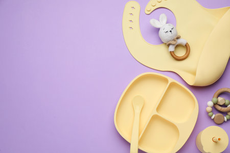 Set of plastic dishware, silicone bib and baby accessories on violet background, flat lay. Space for textの写真素材