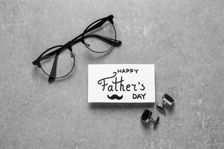 Card with phrase Happy Father's Day, glasses and cuff links on light gray background, flat lay