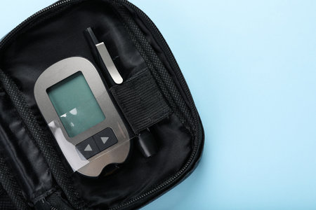 Digital glucometer and lancet pen in bag on light blue background, top view with space for text....
