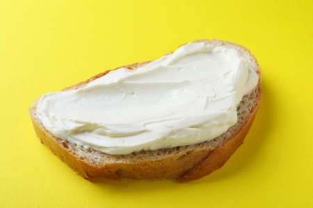 Slice of bread with tasty cream cheese on yellow background, closeupの写真素材