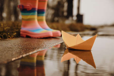 Little girl outdoors, focus on paper boat in puddle