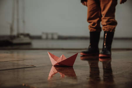 Little boy outdoors, focus on paper boat in puddle