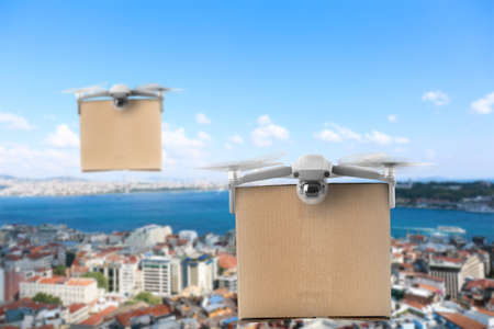 Modern drones with cardboard boxes flying above city on sunny day. delivery serviceの写真素材