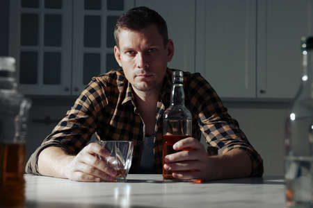 Addicted man with alcoholic drink at table in kitchenの写真素材