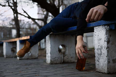 Addicted drunk man with alcoholic drink lying on bench outdoors, closeupの写真素材