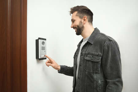 Happy man ringing intercom with camera in entryway