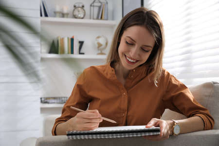 Young woman drawing in sketchbook with pencil at home