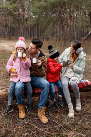 Happy family with cups of hot tea spending time together in the forest