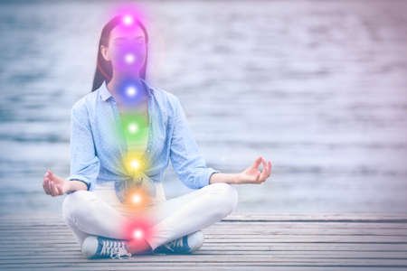 Young woman meditating near the river. Scheme of seven chakras, illustration