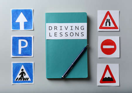 Flat lay composition with workbook for driving lessons and road signs on light gray background....