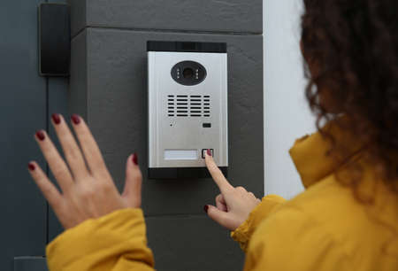 African-American woman ringing intercom while waving to camera near building entranceの写真素材