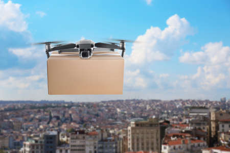 Modern drone with cardboard box flying above city on sunny day. delivery service