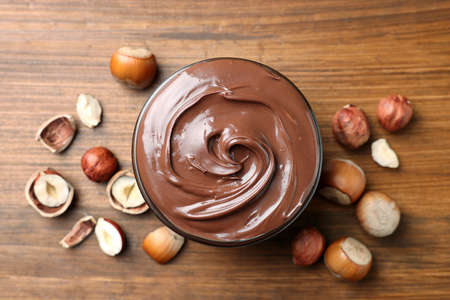 Tasty chocolate hazelnut spread and nuts on wooden table, flat lay