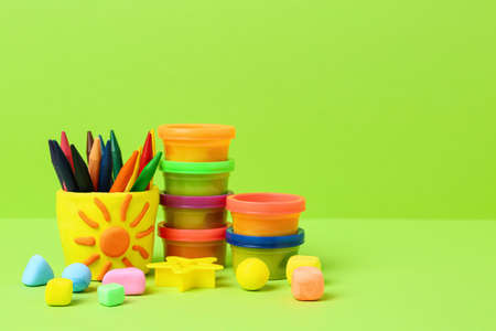 Set of bright play dough with mold and colorful pencils on light green background. Space for text
