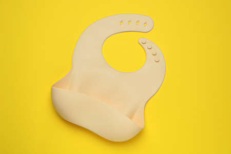 Beige silicone baby bib on yellow background, top view. First food