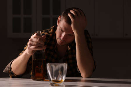 Addicted man with alcoholic drink at table in kitchen