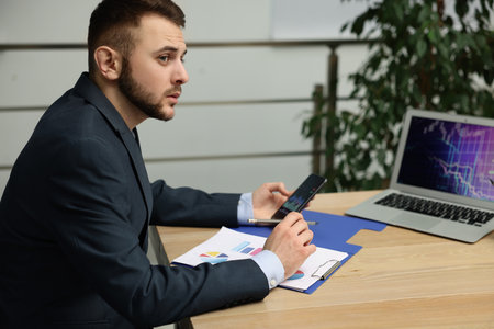 Forex trader working with smartphone and charts at table in office