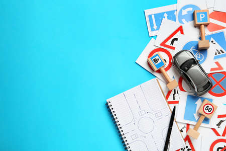 Many different road signs, notebook and toy car on light blue background, flat lay with space for...