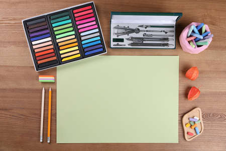 Blank sheet of paper, colorful chalk pastels and other drawing tools on wooden table, flat lay....
