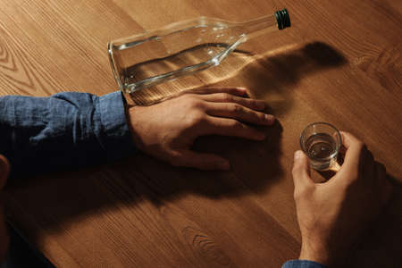 Addicted man with alcoholic drink at wooden table, closeupの写真素材