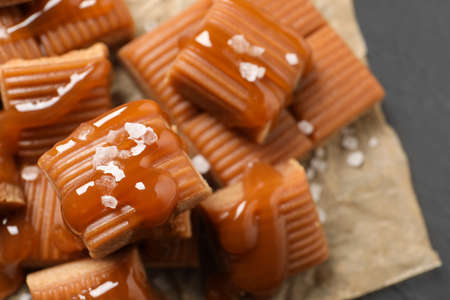 Tasty caramel candies with sauce and sea salt on gray table, closeupの写真素材