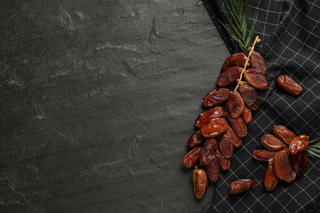 Branches with sweet dried dates and green leaf on black table, flat lay. Space for textの写真素材