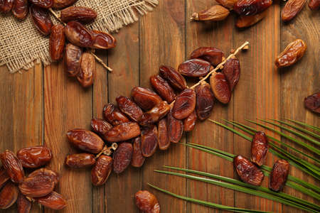 Branches with sweet dried dates and green leaf on wooden table, flat lay